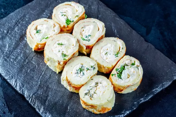 Rollen aus mit Käse und verschiedenen Kräutern gefüllten Eierpfannkuchen auf Schieferplatte