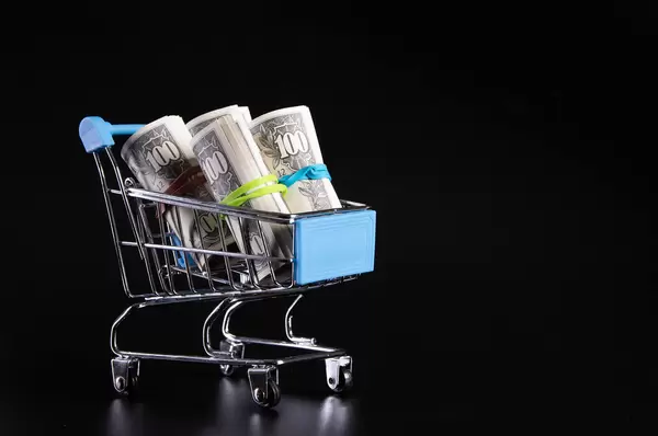 Rolls of dollar banknotes in shopping cart on black background