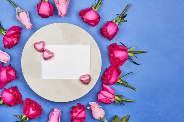 Romantic background with space for a message: card framed by roses and chocolate hearts on blue
