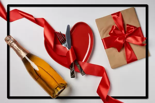 Romantic love background with gift, champagne bottle and red plate with ribbon.