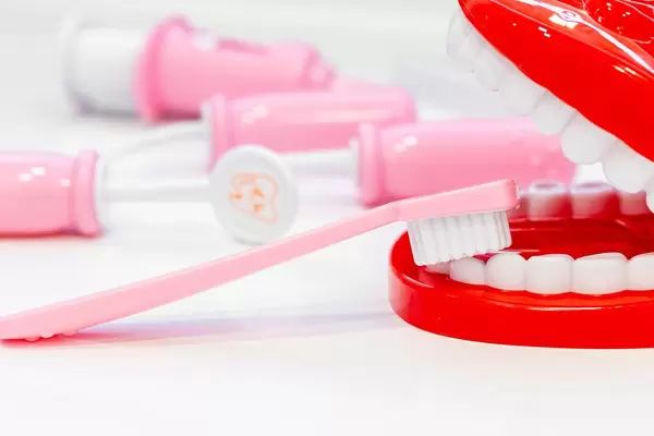 Rosa Zahnbürste putzt die falschen Zähne eines offenen Gebissmodells, mit Zahnarztutensilien im Hintergrund