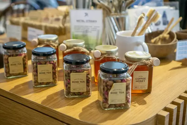 Rose Tea and Coffee Honey in Glass Jars with Bamboo Toothbrushes and Metal Straws in the Background on a Sale Table in a Cafe