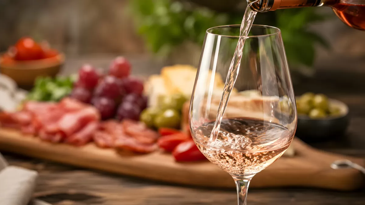 Rosé wird eingeschenkt vor rustikaler Käse-Wurst-Platte