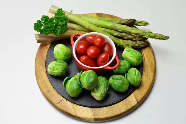 Rosenkohl mit grünem Spargel, Kirschtomaten und Petersilie auf blauem Tonteller