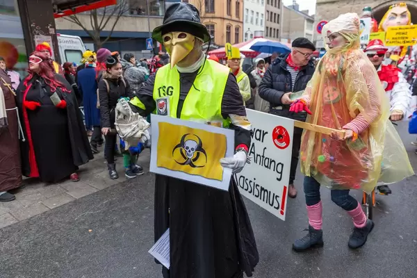 Rosenmontagszug in Köln gegen Rechts: Pappnasen rot-schwarz im Kostüm mit goldener Schnabelmaske, Antifaaufkleber und Totenkopf auf Biohazardlogo