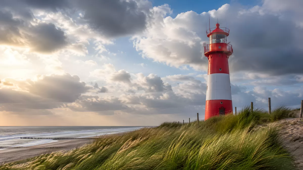 Rot-weißer Leuchtturm an der Nordseeküste bei Bewölkung