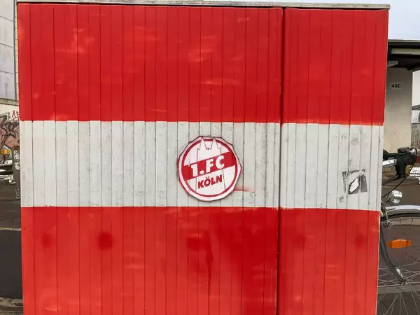 Rot-weiß bemalte Wand mit Aufkleber des Fußballvereins 1. FC Köln mit Fahrrad im Hintergrund