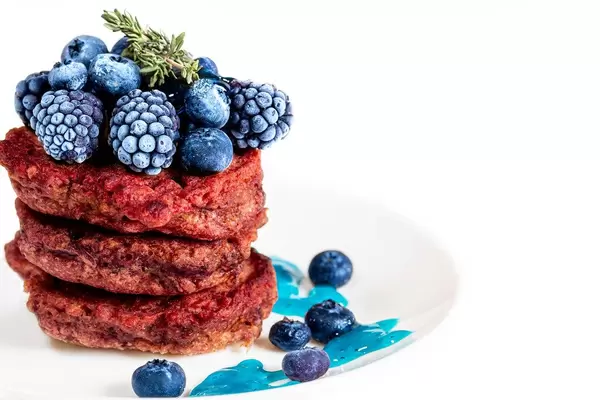Rote Bete Pfannkuchen mit Maulbeeren und frischen Blaubeeren, auf einem weißen Teller