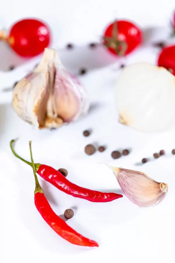 Rote Chilischoten, Cherrytomaten, Knoblauch und schwarze Pfefferkörner auf weißem Hintergrund