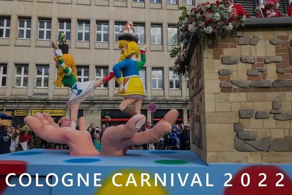 Rote Funken carnival wagon shows dancing girls in costumes on gigantic hands, during rose Monday procession & picture title "Cologne Carnival 2022"