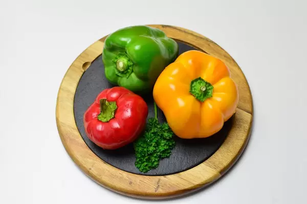 Rote, grüne und gelbe Paprika mit krauser Petersilie auf runder Schieferplatte mit Holzrahmen