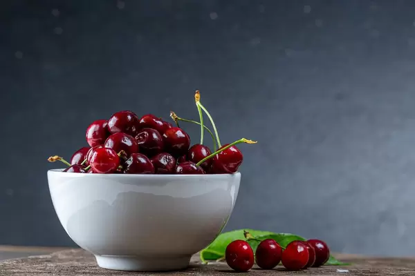 Rote Kirschen an Strängen, in einer weißen Schale, auf einem Holztisch