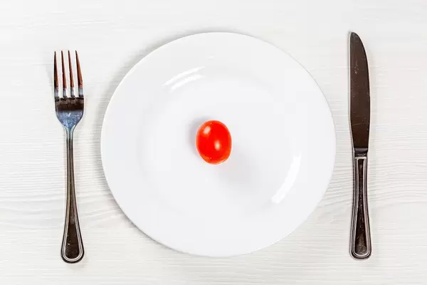 Rote kleine Tomate auf weißem Teller mit Besteck - Konzept der Ernährung