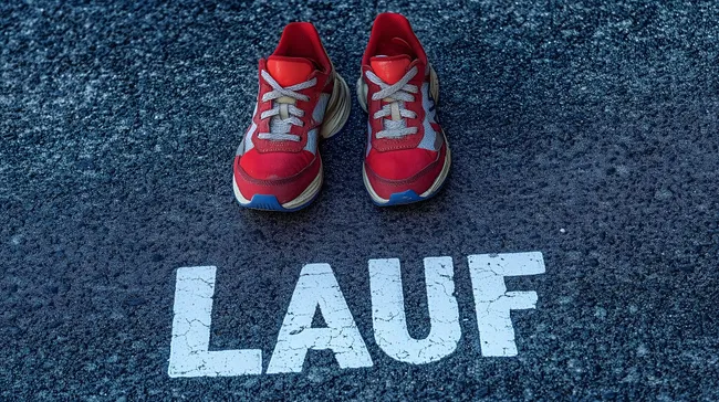Rote Laufschuhe auf Asphaltbahn mit Aufschrift 'Lauf'