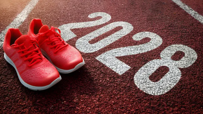 Rote Laufschuhe auf Laufbahn mit Jahreszahl 2028