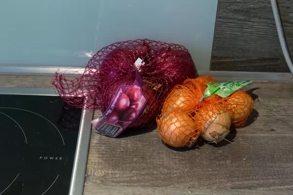 Rote und weiße Zwiebeln in Netz auf Küchenablage neben Herdplatte