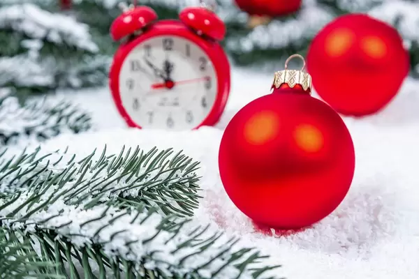 Rote Weihnachtsbaumkugel im Schnee mit Tannenzweigen und rotem Wecker