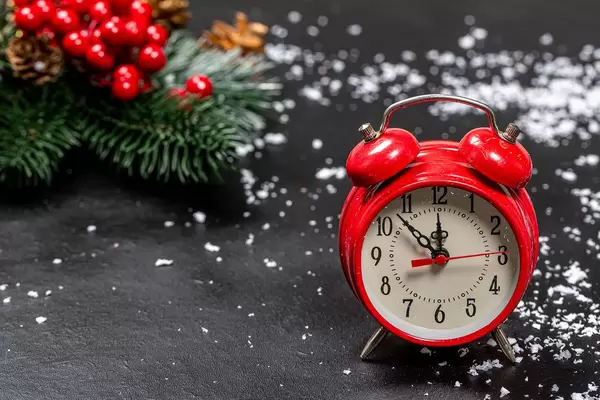 Roter Wecker mit einer Weihnachtsdekoration und Schneeflocken im Hintergrund