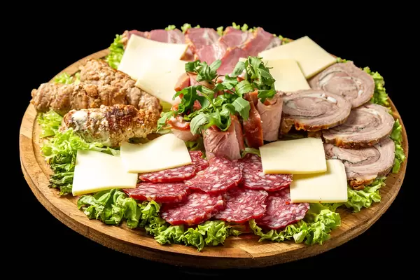 Round board with meat and cheese slices, arugula and lettuce on a black background