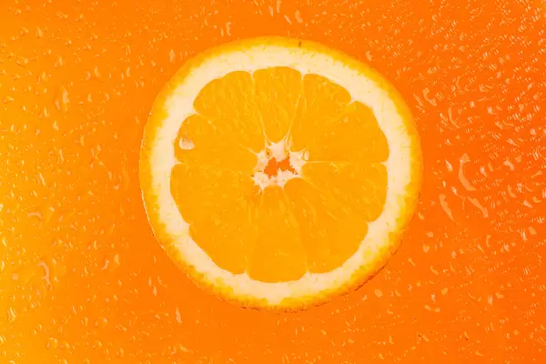 Round orange slice with water drops on orange background