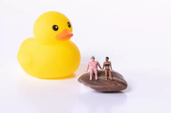 Rubber duck and couple in bathing suit sitting on rock