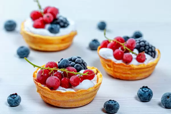 Runde Törtchen mit Sahnecreme und bunten frischen Beeren auf einem weißen Holztisch