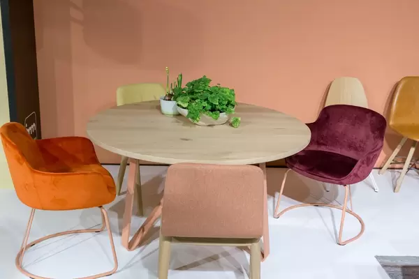 Runder Holztisch mit Blumendekoration umgeben von mit farbigem Stoff bezogenen Stühlen