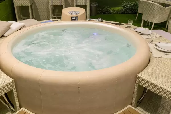 Runder Whirlpool mit beigem Lederüberzug und passendem Beistelltische aus Rattan mit Gedeck