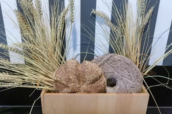 Rundes Sesam-Brot vor Weizenähren, als Landhaus-Dekoration, in einem Holzkorb