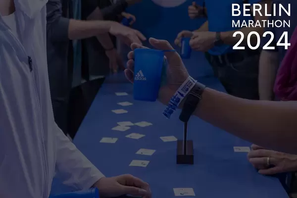 Runners at the Adidas bar with blue beverage cups and the picture title "Berlin Marathon 2024"