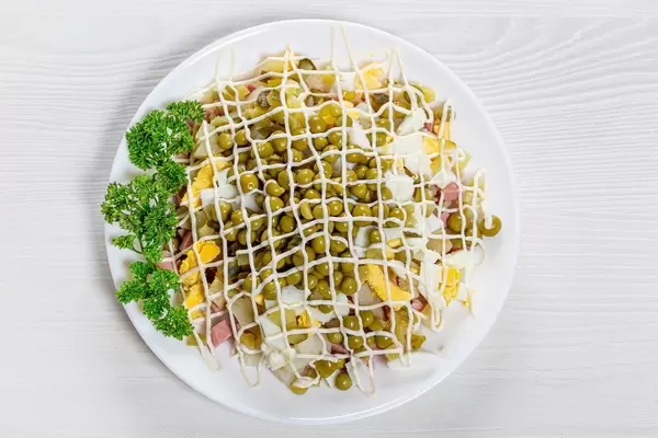 Russischer Oliviersalat mit Eiern, Kartoffeln, Erbsen, Fleisch und Mayonnaise in obene Aufnahme