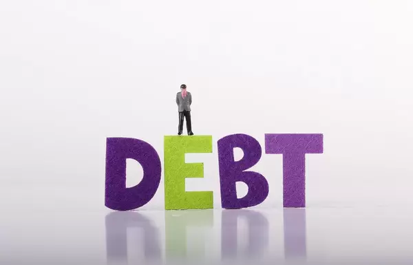 Sad miniature businessman with Debt text on white background