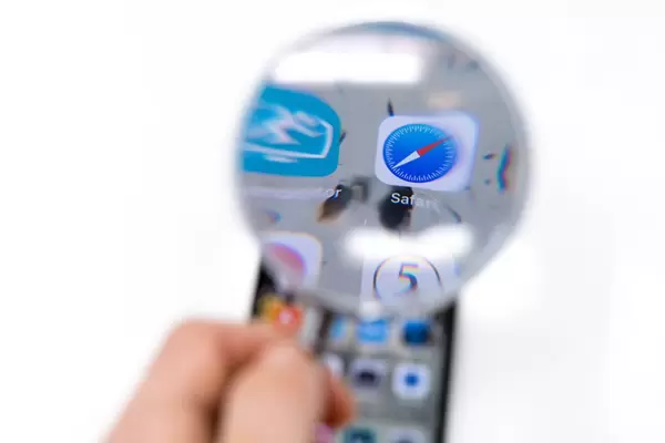 Safari Internet App Logo auf Smartphone durch Lupe betrachtet vor weißem Hintergrund