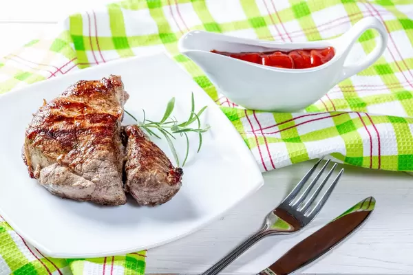 Saftig gegrilltes Rindssteak mit Rosmarin neben Sauciere mit Tomatensoße und Besteck