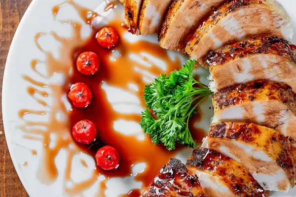 Saftige Scheiben gegrillte Hühnerbrust mit Soße, Tomaten und Petersilie auf einem Teller - Nahaufnahme