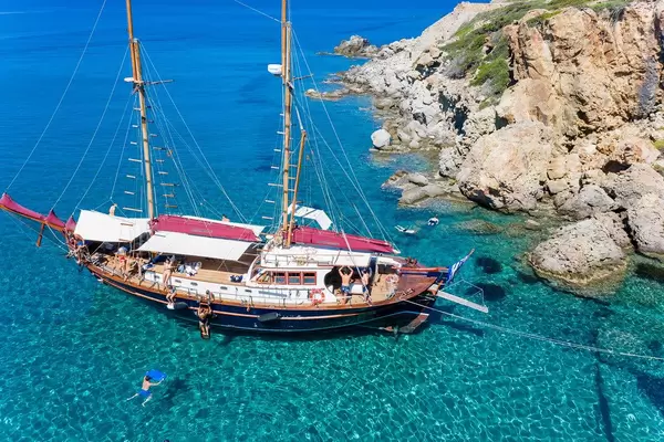 Sailing boat by the coast of Milos in spectacularly clear waters. Tourists swimming and snorkeling