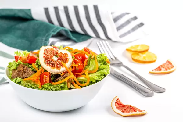 Salad bowl with carrots, lettuce, liver and cherry tomatoes on white background