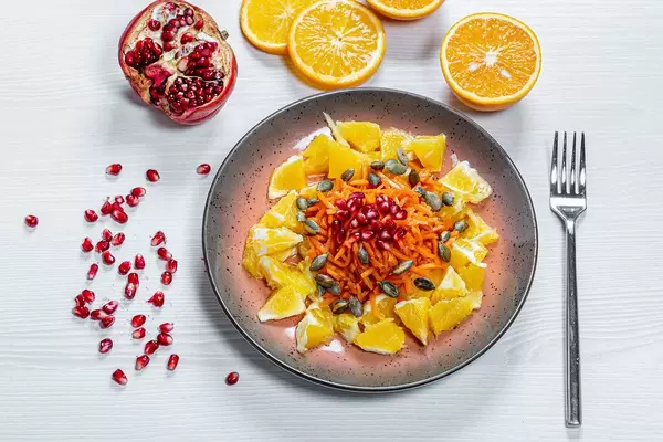 Salad with orange, carrot, pomegranate and pumpkin seeds. Top view. Healthy eating concept