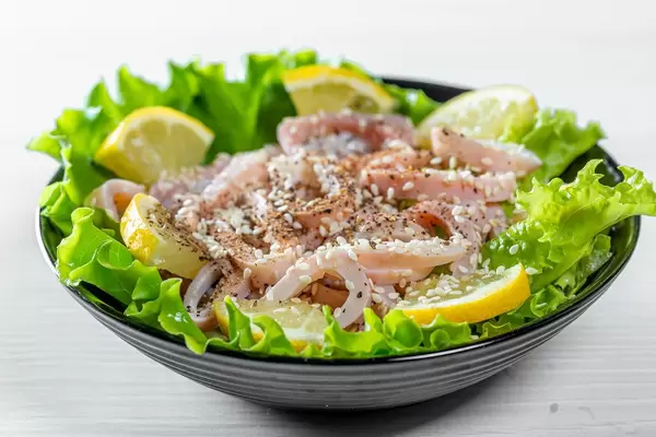 Salad with seafood and lettuce in a black bowl on a white table