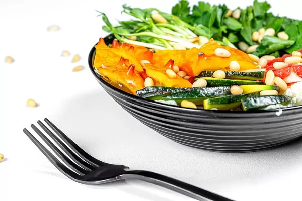 Salad with slices of kiwano, avocado, micro greens and pine nuts in a black bowl with a black fork (Flip 2020)