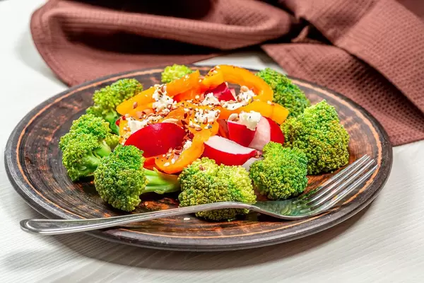 Salat mit Brokkoli, Radieschen, Paprika, Sesam- und Leinsamen im Teller mit einer Gabel