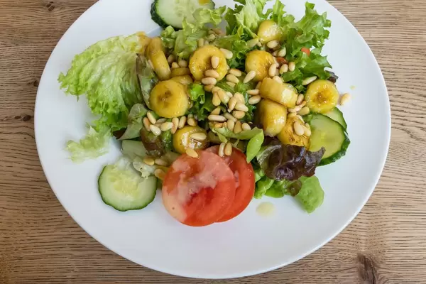 Salat mit Eisbergsalat, Tomate, Gurke, flambierte Banane und Pinienkerne