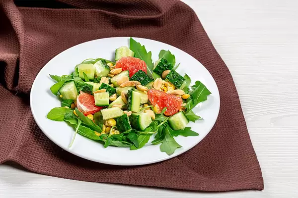 Salat mit Rucola, Gurken, Grapefruit und Nüssen auf einem weißen Teller