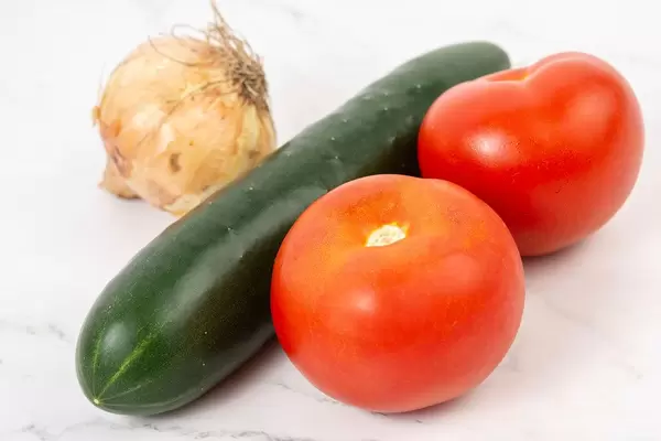 Salatzutaten wie eine Gurke mit Schale, Tomaten und eine Zwiebel, auf einer marmorierten Oberfläche