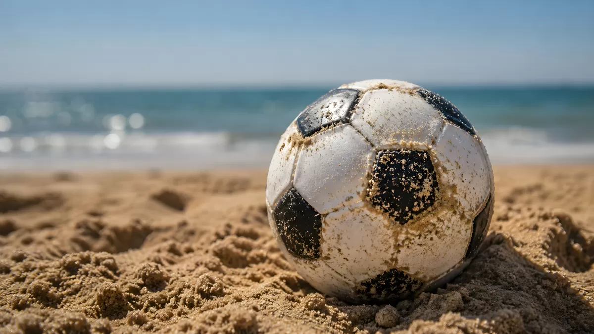 Sandbedeckter Fußball am Strand vor dem Meer