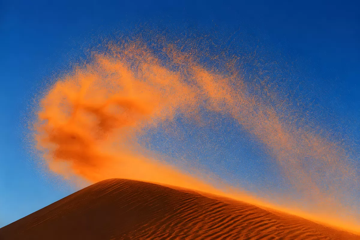 Sandverwehung über einer Düne im Sonnenuntergangslicht