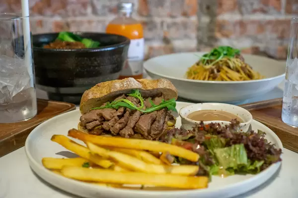 Sandwich with Beef Steak Slices, Arugula and Caramelized Onions with Spaghetti Bolognese, Rice Bowl and Drinks in the Background
