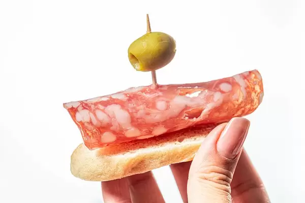 Sandwich with salami and green olive in a woman's hand on a white background (Flip 2019)