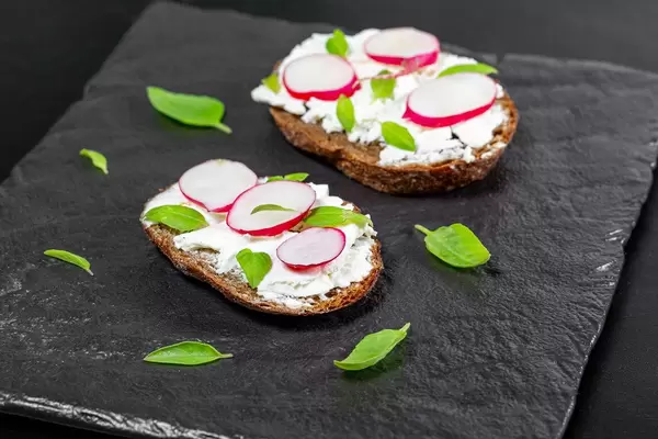 Sandwiches mit Frischkäse, Radieschen und Basilikumblätter auf einem schwarzen Brettn