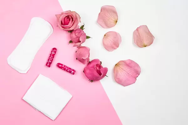 Sanitary pads and fresh rose flower on pink background, women intimate hygiene product